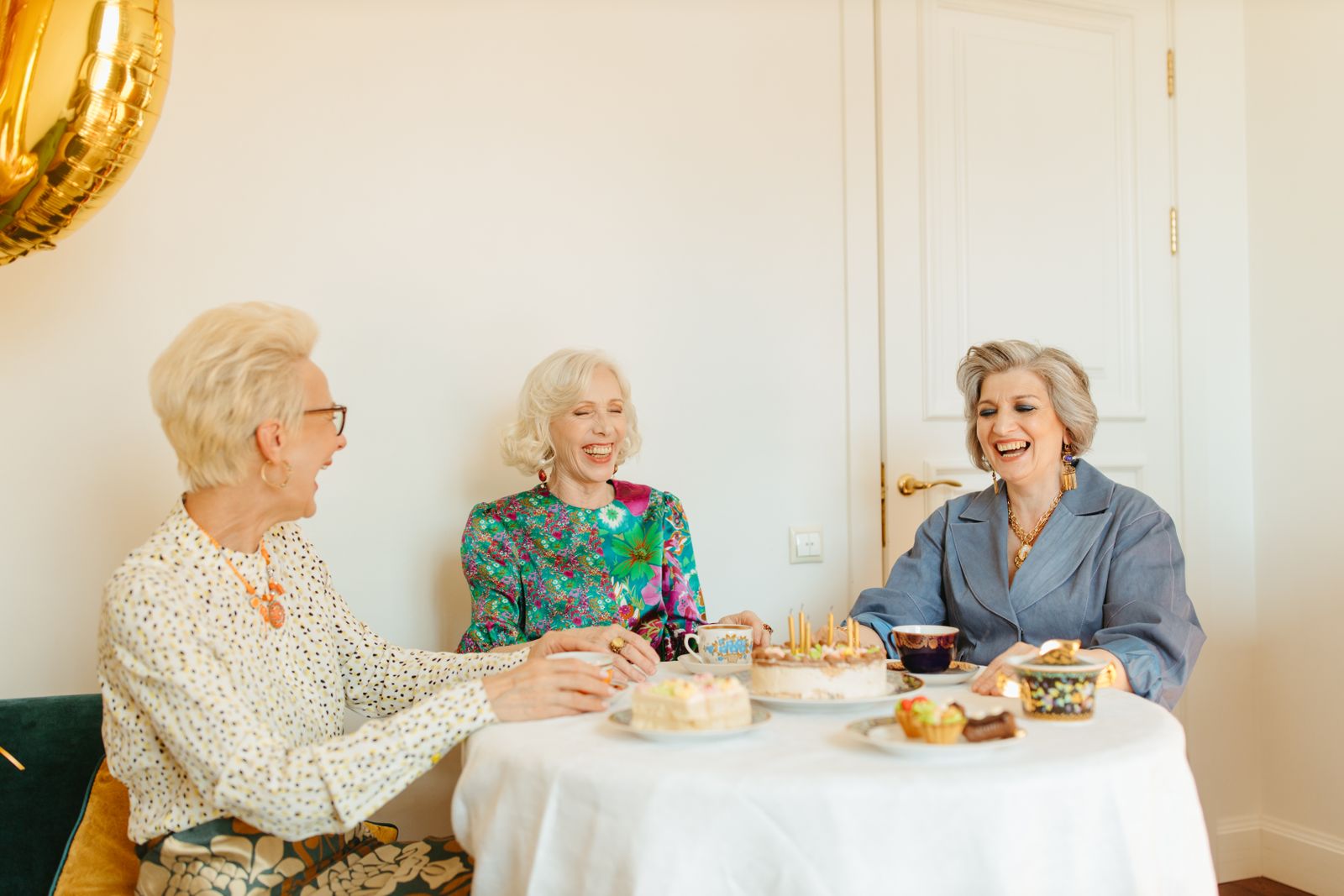 Three friends laughing together over tea and cake